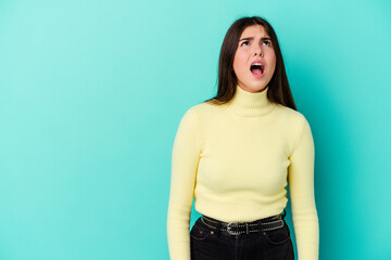 Young caucasian woman isolated on blue background shouting very angry, rage concept, frustrated.