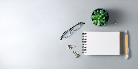 Open notebook, glasses,  bamboo pen and succulent plant on grey desk. Minimal top view gray workplace with copy space