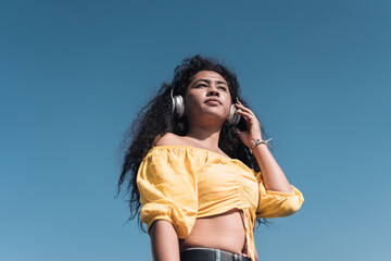 Young African American girl in yellow t-shirt holding her headphones while listening to music.