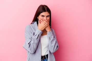 Young caucasian woman isolated on pink background covering mouth with hands looking worried.