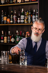 Barman making a cocktail and putting a large ice cube into the glass on the bar counter