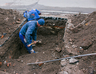 A man handyman digs a trench in the winter in the city by hand with a shovel. Construction...