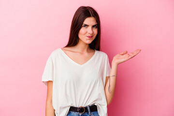 Young caucasian woman isolated on pink background doubting and shrugging shoulders in questioning...
