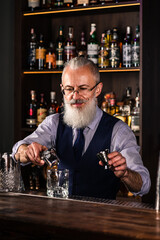 Barman making a cocktail and putting a large ice cube into the glass on the bar counter