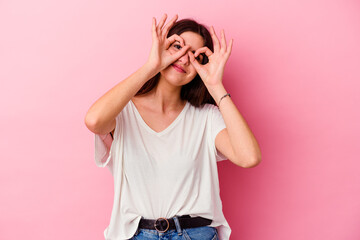 Young caucasian woman isolated on pink background showing okay sign over eyes