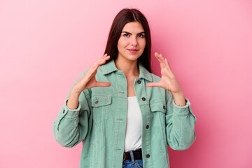 Young caucasian woman isolated on pink background holding something with palms, offering to camera.