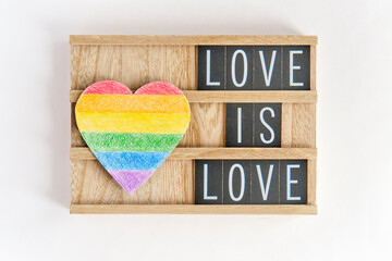 Paper heart painted with colored pencils like a LGBT flag and text Love is Love on a wooden stand