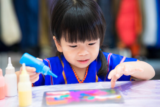 Asian girl doing crafts with watercolor. Child was holding blue bottle with watercolor inside. Children diligently put paint on pattern. Kids enjoy making art. Practice meditation for young children.