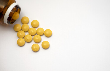 Iron is a very valuable and one of the most important minerals in our body. Front view of a brown bottle with several yellow iron tablets spilling onto on a white background