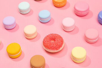 Sweet and colorful french macarons with a doughnut on pink background