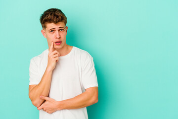 Young caucasian man isolated on blue background looking sideways with doubtful and skeptical expression.