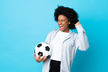 Young African American woman isolated on blue background with soccer ball celebrating a victory