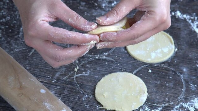 Pelmeni dumplings making process: Woman's hand shaping round pelmeni dough stuffed with chicken filling. Gluten free recipe for traditional Russian cuisine. Floured wooden surface, handmade dumplings.