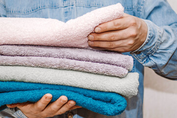 Man holds a stack of fresh terry towels. Organization and cleaning of the house. Storage and housekeeping concept