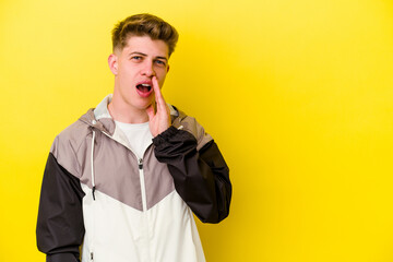 Young caucasian man isolated on yellow background shouts loud, keeps eyes opened and hands tense.