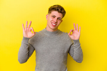 Young caucasian man isolated on yellow background cheerful and confident showing ok gesture.