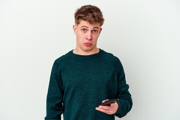 Young caucasian blonde man using a telephone isolated on white background shrugs shoulders and open...