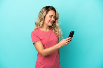 Fototapeta premium Young Brazilian woman isolated on blue background sending a message or email with the mobile
