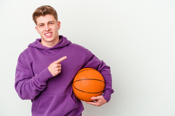 Obraz premium Young caucasian man playing basketball isolated background smiling and pointing aside, showing something at blank space.