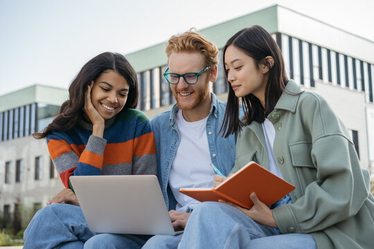 Group of multiracial university students using laptop, studying, exam preparation, education concept. Young smiling colleagues meeting, cooperation, planning project, working together outdoors 