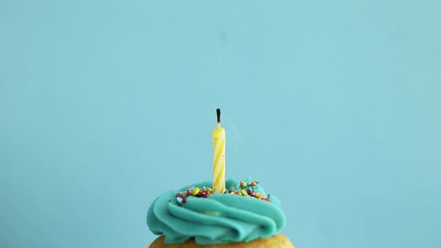 Birthday greetings concept. Blow out candle on muffin, cupcake. Blue background