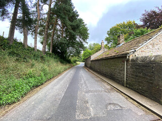 Looking up the, B6160 road, with wild plants, stone buildings, and a cloudy sky near, Bolton Abbey, Skipton, UK