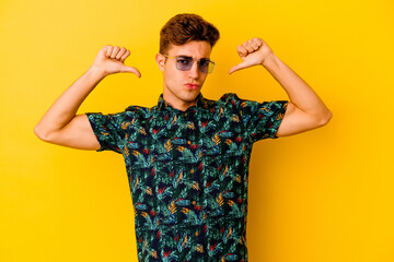 Young caucasian man wearing a Hawaiian shirt isolated on yellow background feels proud and self...