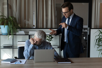 Angry young Caucasian male boss or CEO lecture scold middle-aged employee at workplace. Mad 30s businessman have fight quarrel with senior worker, correct mistakes errors. Discrimination concept. - obrazy, fototapety, plakaty