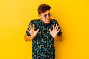 Young caucasian man wearing a Hawaiian shirt isolated on yellow background rejecting someone...