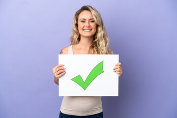 Naklejka premium Young Brazilian woman isolated on purple background holding a placard with text Green check mark icon with happy expression