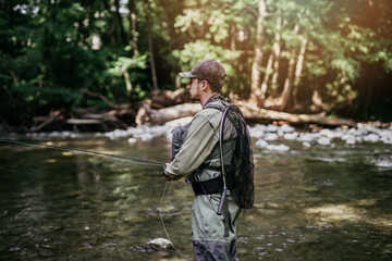 Young adult man is fishing alone on fast mountain river. Active people and sport fly fishing concept.
