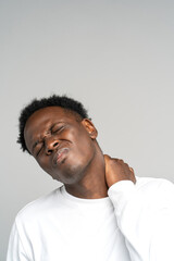 Obraz premium Unhappy Black man suffering from neck pain, pinched nerve in her back. African male has spinal problem, shoulder stiffness, muscle inflammation, rheumatoid pain isolated on studio grey background.