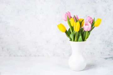 Tulips flower bouquet in white ceramic vase at light background.
