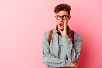 Young student man isolated on pink background is saying a secret hot braking news and looking aside