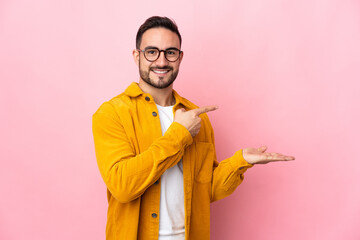 Young caucasian handsome man isolated on pink background holding copyspace imaginary on the palm to...