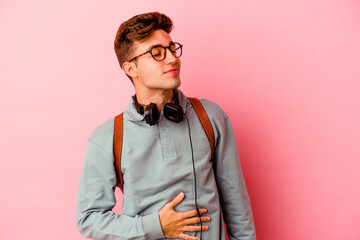 Young student man isolated on pink background touches tummy, smiles gently, eating and satisfaction concept.