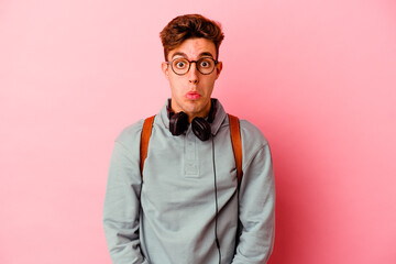 Young student man isolated on pink background shrugs shoulders and open eyes confused.