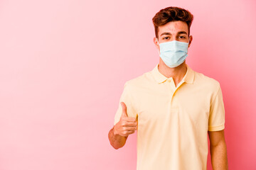 Young caucasian man wearing a protection for coronavirus isolated on pink background smiling and raising thumb up