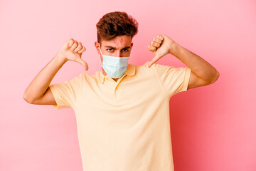 Young caucasian man wearing a protection for coronavirus isolated on pink background showing thumb down and expressing dislike.