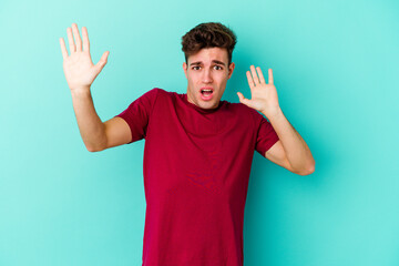 Young caucasian man isolated on blue background being shocked due to an imminent danger