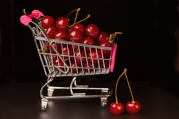 A supermarket cart is filled with ripe red cherries on a black background.