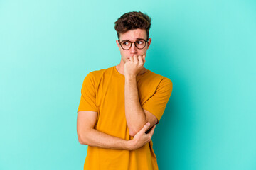 Young caucasian man isolated on blue background biting fingernails, nervous and very anxious.