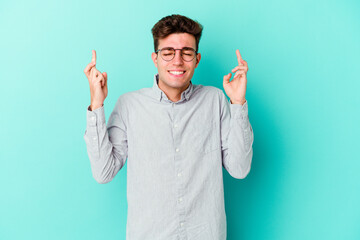 Young caucasian man isolated on blue background crossing fingers for having luck