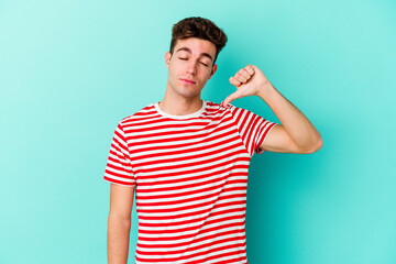 Young caucasian man isolated on blue background showing a dislike gesture, thumbs down. Disagreement concept.