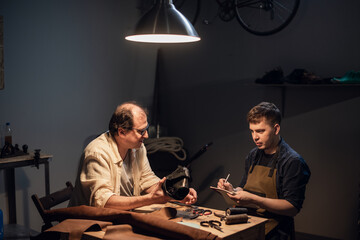 father-shoemaker prepares a successor in the family business of manual production of shoes in the workshop in his house