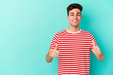 Young caucasian man isolated on blue background smiling and raising thumb up
