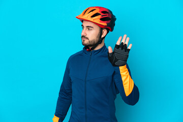 Young cyclist man isolated on blue background making stop gesture and disappointed - obrazy, fototapety, plakaty