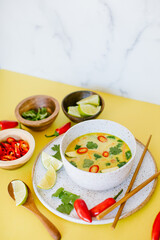 spicy thai coconut soup on a yellow background with chiles, lime and cilantro as garnish