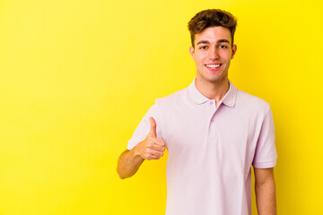 Young caucasian man isolated on yellow background smiling and raising thumb up