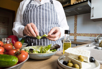 Woman prepare fresh greek salad in the kitchen .